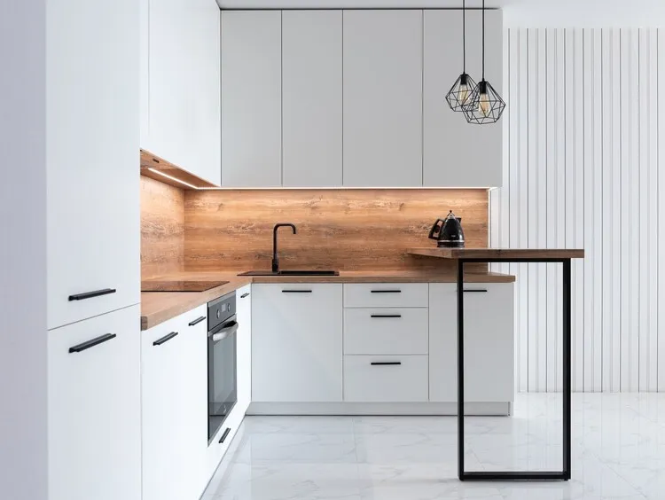 Tủ bếp PVC màu trắng kết hợp với ốp bếp và mặt bàn giả đá vân gỗ tạo nên nét độc đáo, mới mẻ cho gian bếp. 