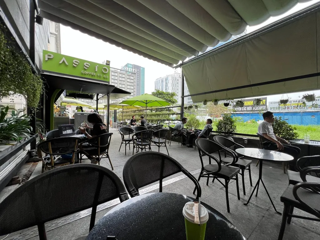 Chỗ ngồi của quán cafe được bố trí ngoài trời, với mái che và cây xanh xung quanh tạo không khí thoáng mát