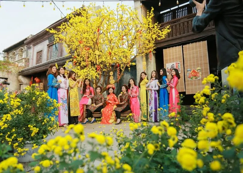 Dưới khoảng trời trong xanh, chị em phụ nữ rạng rỡ trong tà áo dài truyền thống, đang vui vẻ tạo dáng bên cạnh cành hoa mai. Nụ cười của họ như những bông hoa đua sắc, tô điểm cho mùa xuân thêm rực rỡ