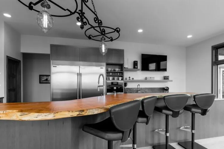 Quầy bar với mặt bàn là gỗ nguyên tấm, thiết kế cong nhẹ đầy tinh tế nổi bật trên nền nội thất tối màu.
